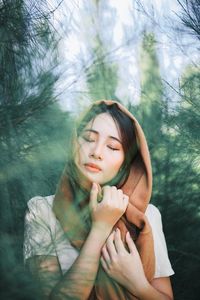 Young woman with eyes closed against trees