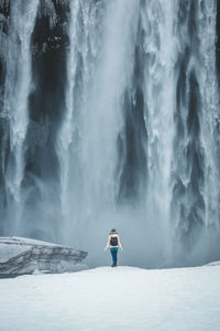 Rear view of woman standing against waterfall