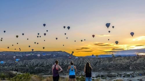 Rear view of women against hot air balloons in mid-air during sunrise in goreme