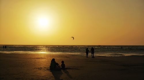 Silhouette people on beach against sky during sunset