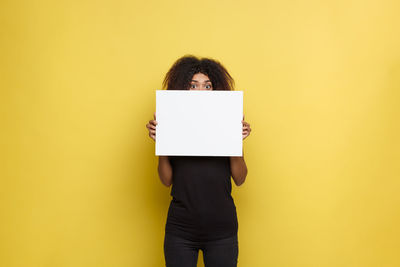 Portrait of woman holding blank paper against yellow background