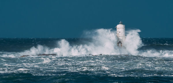 Waves splashing on shore against clear sky