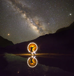 Rear view of man spinning wire wool while standing by lake against star field at night