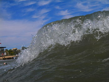 Sea waves splashing on shore against sky