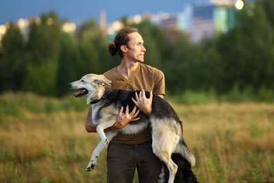 Smiling man carrying dog while standing on grassy land