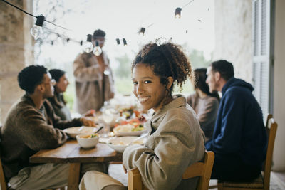 Portrait of smiling young woman sitting at dining table with friends during dinner party