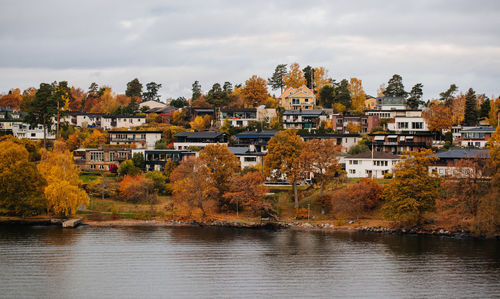 Houses by river against sky during autumn