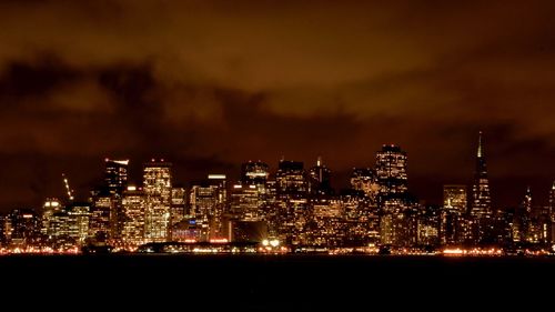 Illuminated buildings by sea against sky at night