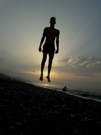 Full length of silhouette man jumping on beach against sky during sunset