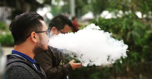 Side view of mid adult man smoking while standing outdoors