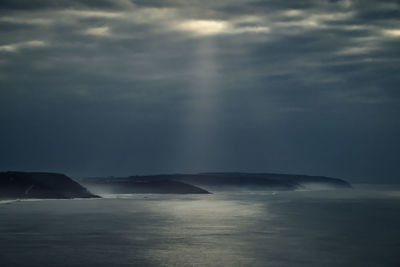 View of the coast near nazaré in portugal while the sun shines dramatically through dark clouds.