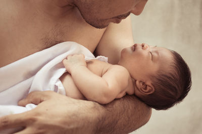 Midsection of shirtless father holding newborn son against wall