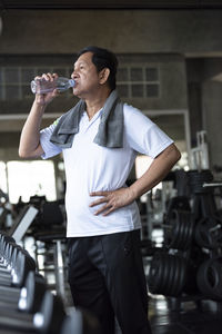 Man drinking water while standing in gym