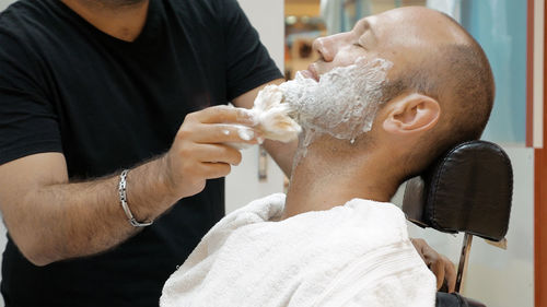 Barber applying shaving cream on mature man in salon