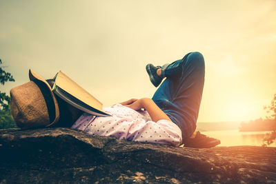 Side view of woman lying on rock against sky