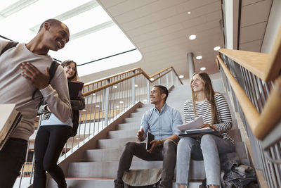 Happy multi-ethnic friends talking while sitting on staircase in university