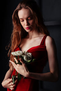 Beautiful young woman wearing red rose against black background