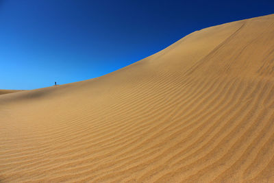 Sand dunes in desert against clear blue sky