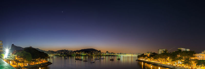 River by illuminated city against clear sky at night