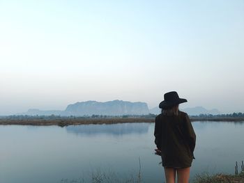 Rear view of man standing by lake against sky