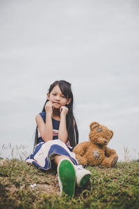 Full length of girl with toy sitting on land against sky