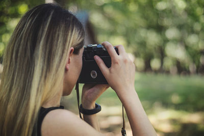 Young woman photographing through camera while standing outdoors