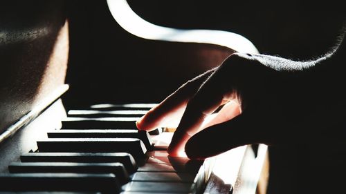 Close-up of hand playing piano in darkroom