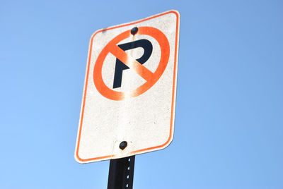 Low angle view of road sign against clear blue sky