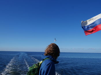 Side view of man standing by russian flag against sea