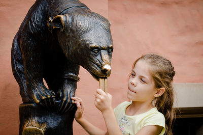 Girl holding animal statue while standing against wall