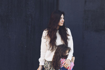 Mother and daughter standing against wall