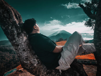 Woman sitting on rock against sky