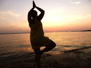 Silhouette woman stretching on beach during sunset