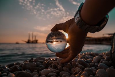 Close-up of hand holding crystal ball at beach during sunset