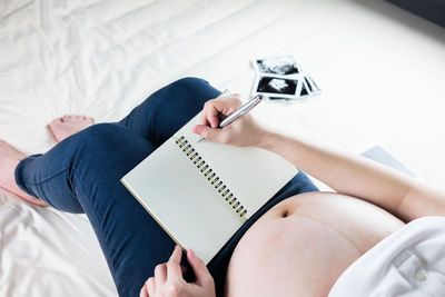 Low section of woman reading book on bed at home