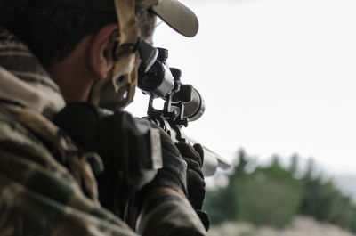 Close-up of soldier aiming with gun against clear sky