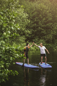 Senior woman and man high-fiving while learning paddleboarding in sea during sup course