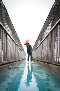 Girl standing on wet footbridge against clear sky