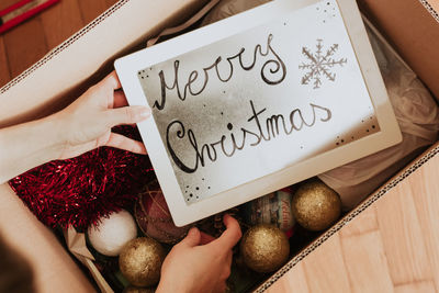 Crop person taking frame with merry christmas inscription from box person