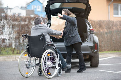 A woman helps aphysical disabled person to get into the car.