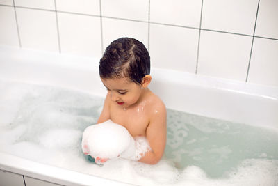 Boy with big eyes a caucasian child bathes in a white bath with foam