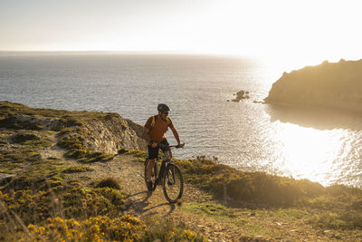Mature male sportsperson cycling on cliff by sea