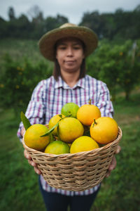 Portrait of woman wearing hat while holding fruits in basket