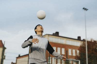 Teenage boy playing with sports ball against sky