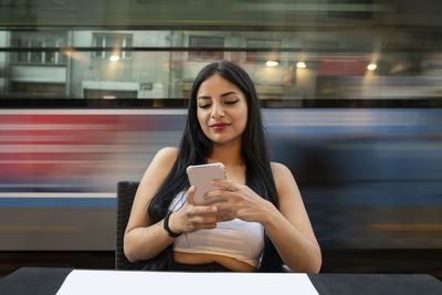 Young woman using mobile phone while sitting at table in cafe during dusk