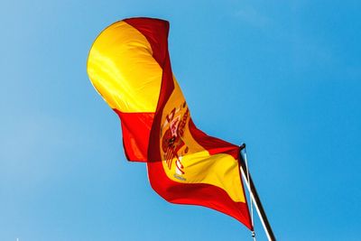 Low angle view of spanish flag fluttering against blue sky