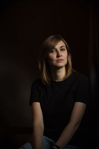 Portrait of woman sitting against black background