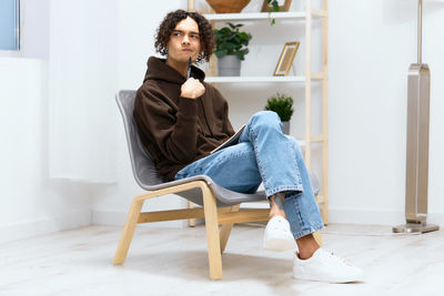 Young man holding pen sitting on chair at home