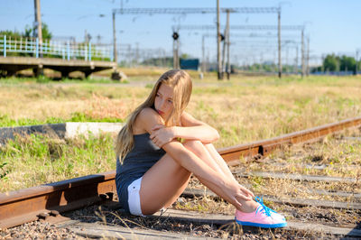 Pensive teenage girl sitting on railroad tracks