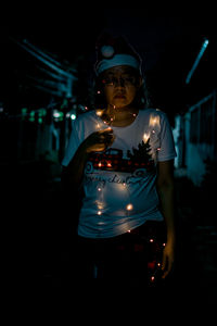 Portrait of woman standing against illuminated string lights at night